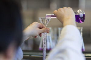 Eine Person schüttet eine lila Flüssigkeit aus einem Erlenmeyerkolben in einen gläsernen Trichter.