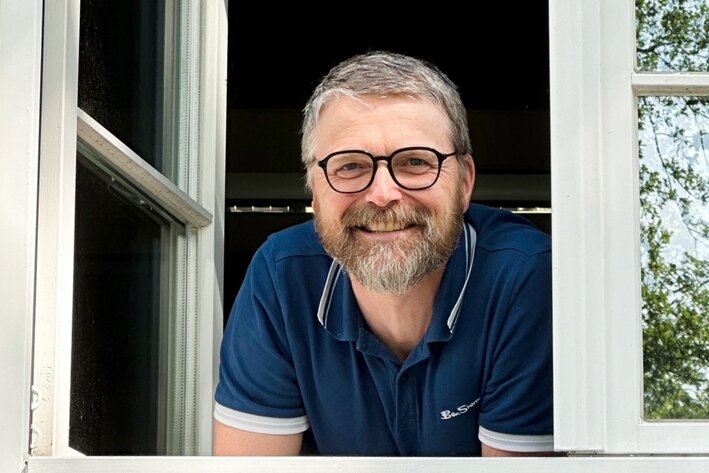 Mann schaut lächelnd aus dem Fenster