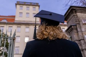 Frau mit Doktorhut blickt auf ein Gebäude der Hochschule