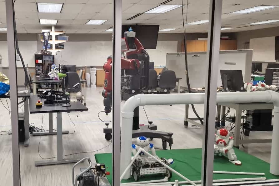 Blick in ein Labor mit humanoiden Robotern, Schreibtischen und technischen Gerätschaften