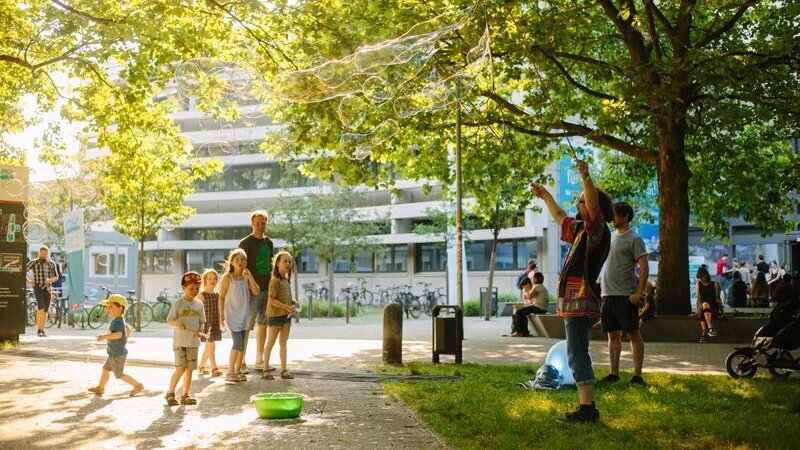 Kinder und Erwachsene sehen dabei zu, wie jemand riesige Seifenblasen macht auf dem grünen Campus der BHT