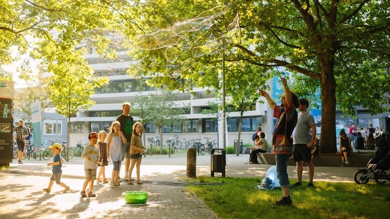 Kinder und Erwachsene sehen dabei zu, wie jemand riesige Seifenblasen macht auf dem grünen Campus der BHT