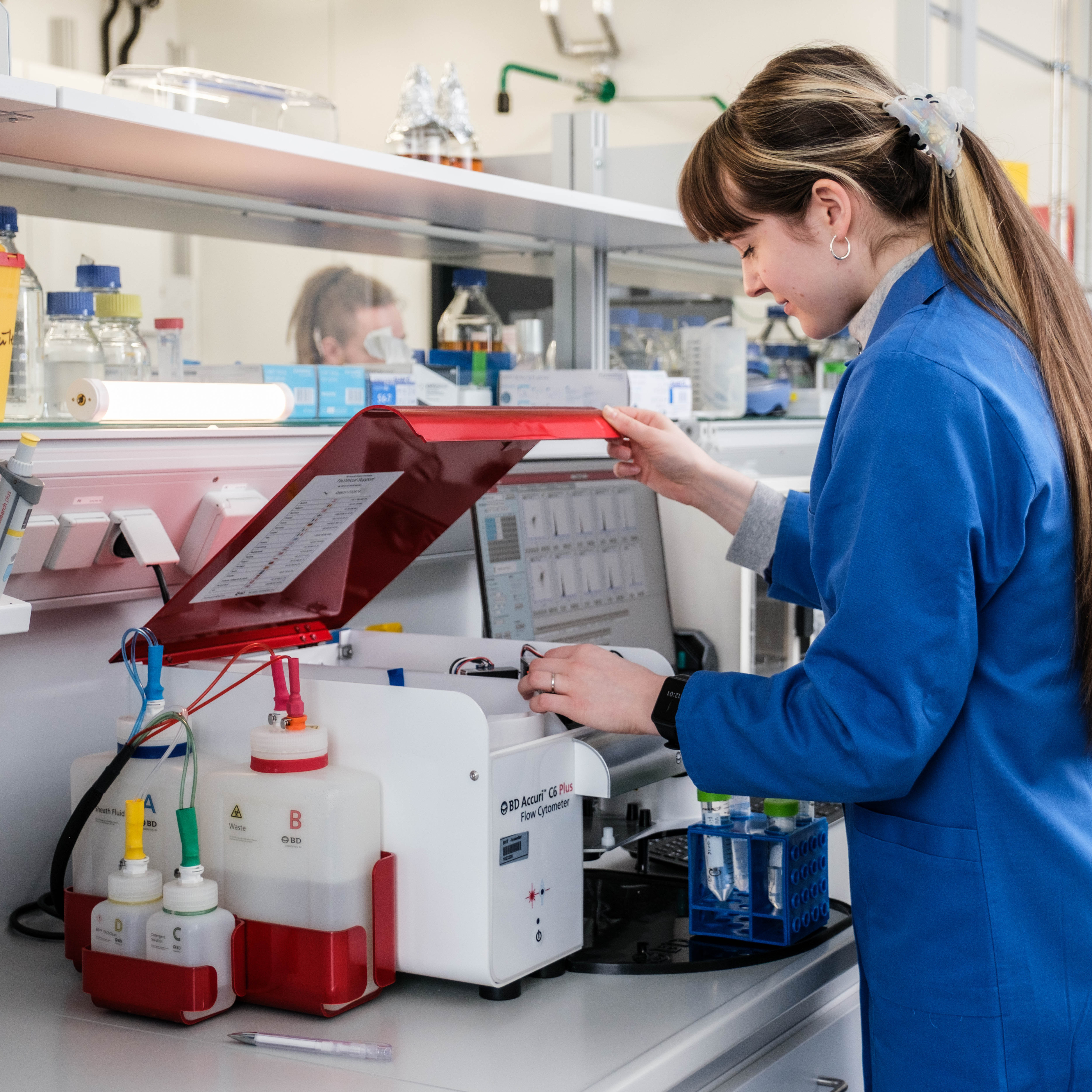 Frau in blauem Kittel an einem Durchflusszytometer im Labor für Mikrobiologie