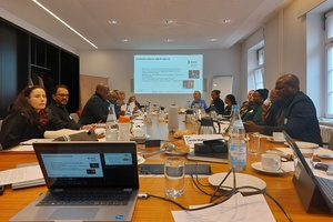 Personen sitzen an Konferenztisch und schauen Präsentationen an