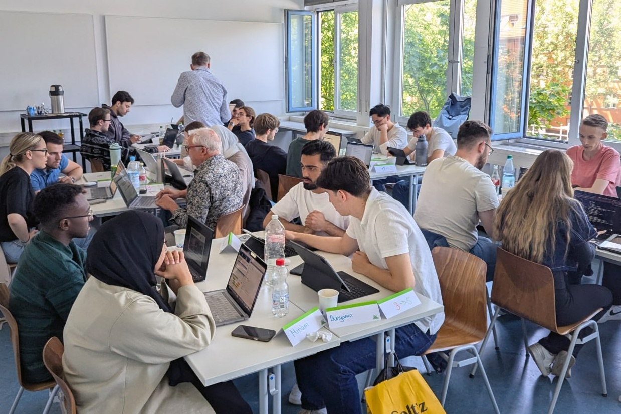 Studierende arbeiten mit Laptops in Gruppen an Tischen in einem Seminarraum