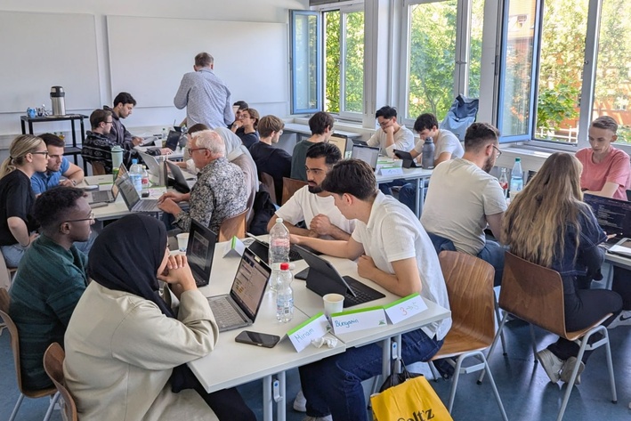 Studierende arbeiten mit Laptops in Gruppen an Tischen in einem Seminarraum