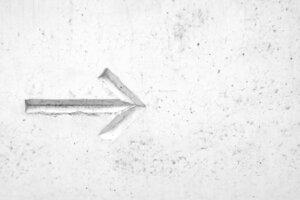 Eine weiße Wand, in die ein nach rechts weisender Pfeil geritzt ist.