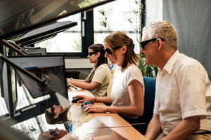 Drei Personen sitzen vor Rechnern, auf einem Bildschirm ist eine Luftbildaufnahme erkennbar