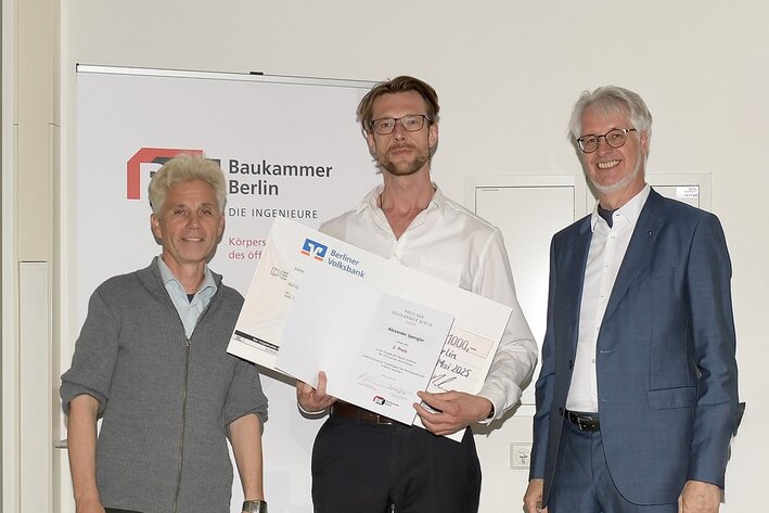 Drei Männer stehen nebeneinander. Der Mann in der Mitte hält eine Urkunde und einen großen Scheck in den Händen.