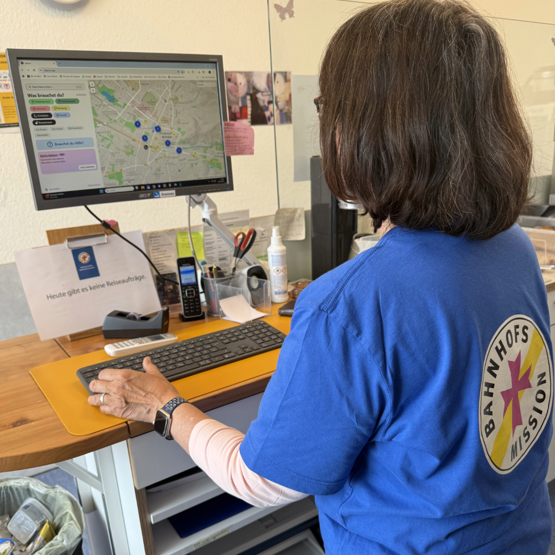 Eine Frau, die ein T-Shirt der Bahnhofsmission trägt, steht an einem Computer