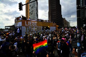 Demonstrationszug in der Innenstadt von Berlin: Eine Person schwenkt eine Regenbogenflagge, ein Bus trägt die Aufschrift „Liebe tut der Seele gut“.