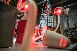 Zylinderförmiger Tank, an den Schläuche angeschlossen sind und auf den rotes Licht aus Strahlern gerichtet ist