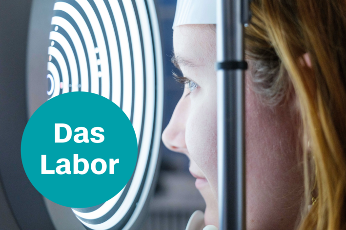 Frau Blickt in einen Videotopographen, ein gerät mit runder Öffnung mit vielen Lichtkreisen; Text: Das Labor