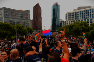 Eine große Menschenmenge beim Potsdamer Platz in Berlin. Viele schwenken Regenbogenfahnen.