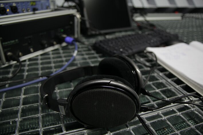Kopfhörer liegen auf einem Tisch. Dahinter sind technische Geräte zu erkennen.
