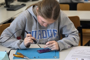 Mädchen sitzt an einem Tisch im Labor und lötet
