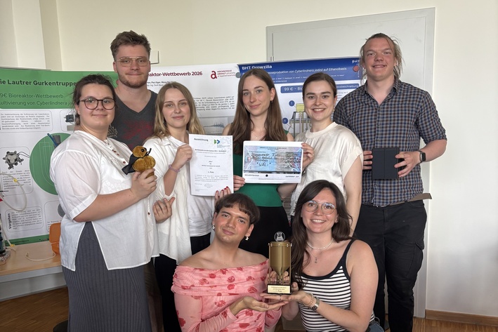 Gruppenfoto von 8 Studierenden, die Urkunden und eine Trophäe in die Kamera halten