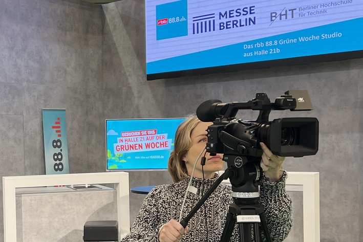 Vor einem Messerstand blickt eine Frau in eine Filmkamera, eine weitere Frau steht daneben und blickt zu ihr