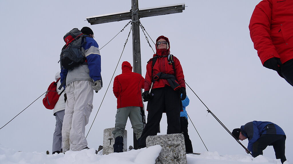Menschen in Winterkleidung auf verschneiten Berggipfel mit Gipfelkreuz