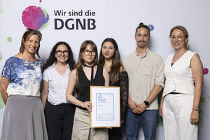 Sechs Personen posieren für ein Foto, die Zweite von Links hält eine gerahmte Urkunde in der Hand