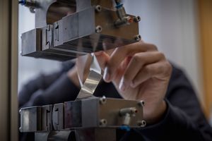 Eine Hand hantiert mit einem Stück Metall und einer Presse in einer Werkstatt.
