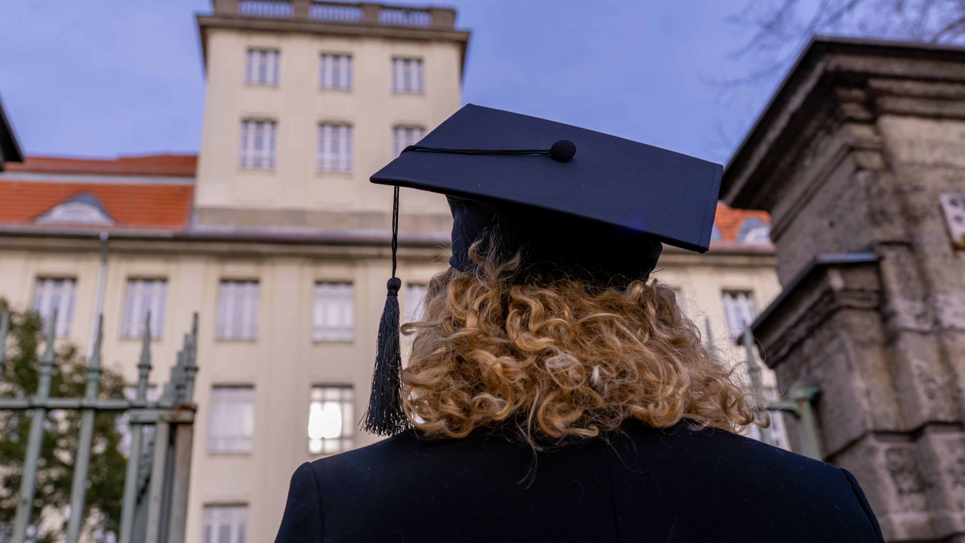 Rückansicht einer Frau mit Doktorhut vor dem Haus Beuth der BHT
