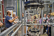 Menschen im Labor. Im Vordergrund ein Glaszylinder mit Popcorn