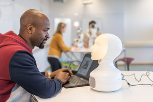 Ein Mann und ein Roboter-Kopf sitzen sich am Tisch gegenüber