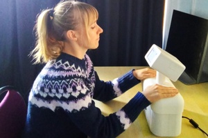 Frau sitzt mit geschlossenen Augen an einem Tisch, auf dem ein kleiner Roboter steht, auf den sie beide Hände gelegt hat