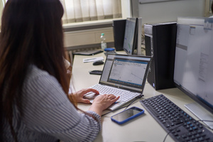 Eine Person sitzt an einem Tisch und arbeitet am Laptop.