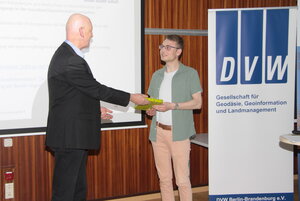 Ein Mann bekommt von einem anderem Mann auf einer Bühne ein Buch überreicht