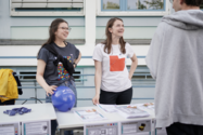 zwei lachende Frauen stehen an einem Stand und unterhalten sichmit einem Mann