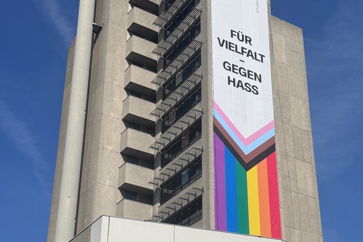 Am Turm des Hauses Grashof auf dem BHT-Campus hängt ein Banner mit der Aufschrift Für Vielfalt - gegen Hass und Progress-Pride-Flagge 