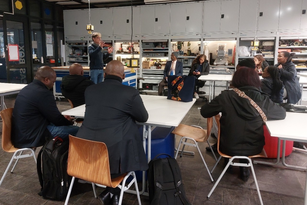 Menschen sitzen an Tischen in Makerspace und lassen sich Geräte und Projekte erklären