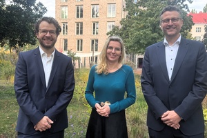 Zwei Männer im Anzug stehen links und recht neben Präsidentin Julia Neuhaus auf dem grünen BHT-Campus
