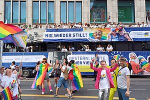 Truck mit vielen feiernden Personen, davor bunt gekleidete Menschen, die tanzen