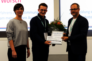 Ein junger Mann erhält eine Urkunde von einem Mann und einer Frau auf einer Bühne.