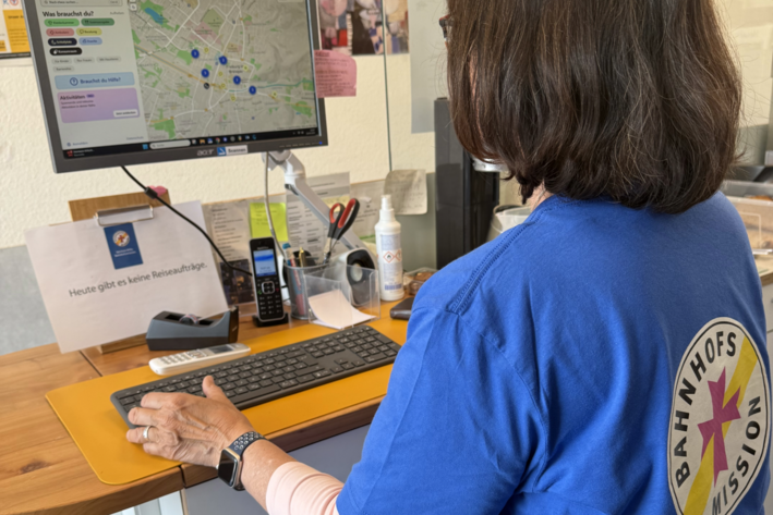 Eine Frau, die ein T-Shirt der Bahnhofsmission trägt, steht an einem Computer