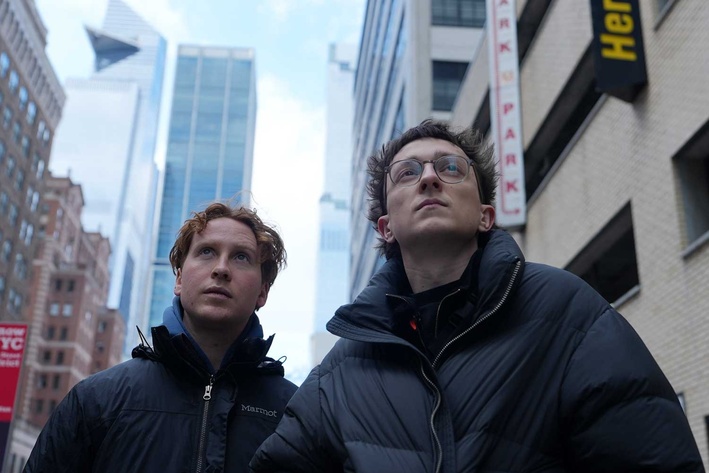 Zwei Junge Männer stehen auf einer Straße zwischen hohen Häusern und blicken in die Ferne