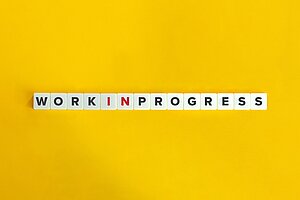 Scrabble-Steine liegen auf einem gelben Untergrund. Sie bilden den Satz: Work in Progress