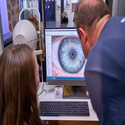 Ein Mann und eine Frau gucken auf einen Monitor, auf dem ein Auge abgebildet ist