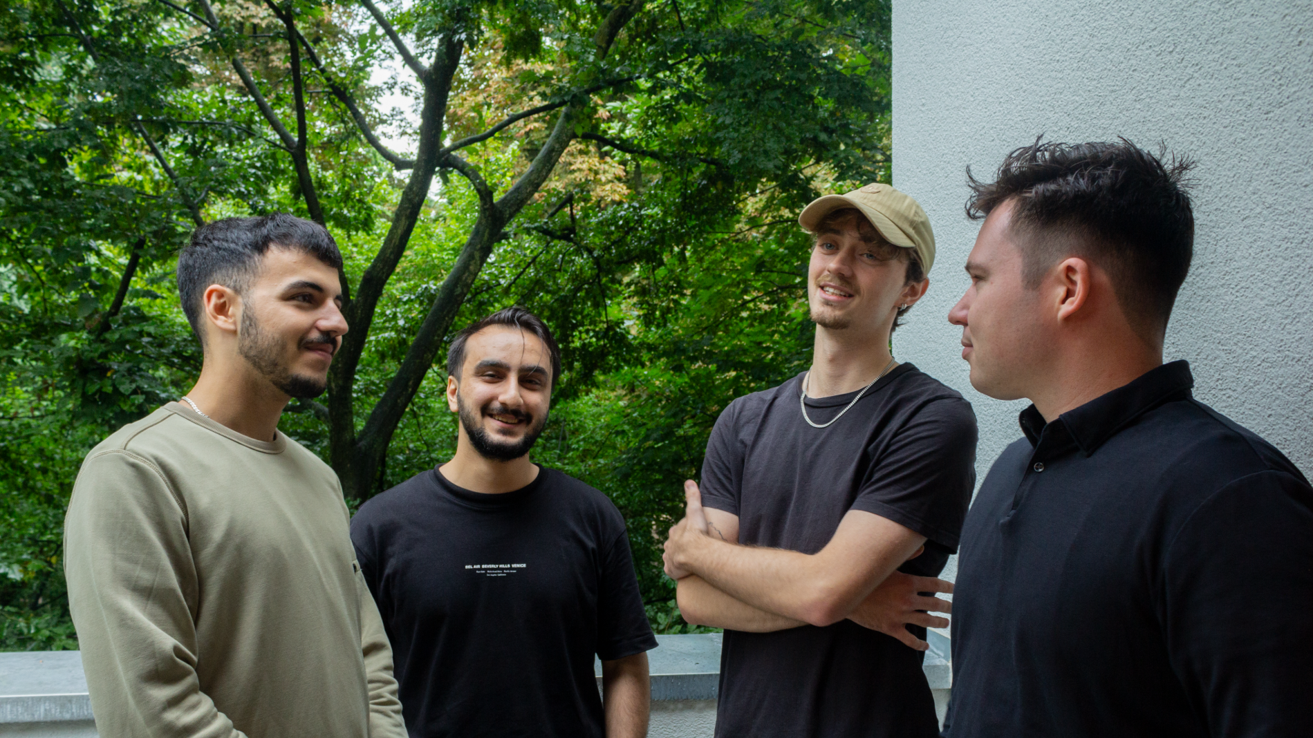 Vier Männer stehen locker auf einem Balkon mit Blick ins Grüne