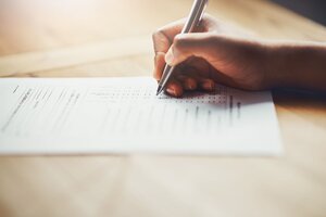 Auf einem Tisch liegt ein Formular, darüber die Hand einer Person, die einen Stift hält.