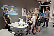 Ein Mann erklärt Besucherinnen eine Projektion an der Wand