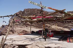 improvisierter Unterstand auf einem felsigen Berg aus Ästen und Stoffen, daran ein Schild mit der Aufschrift "Welcome"