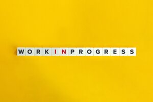 Scrabble-Steine liegen auf einem gelben Untergrund. Sie bilden den Satz: Work in Progress