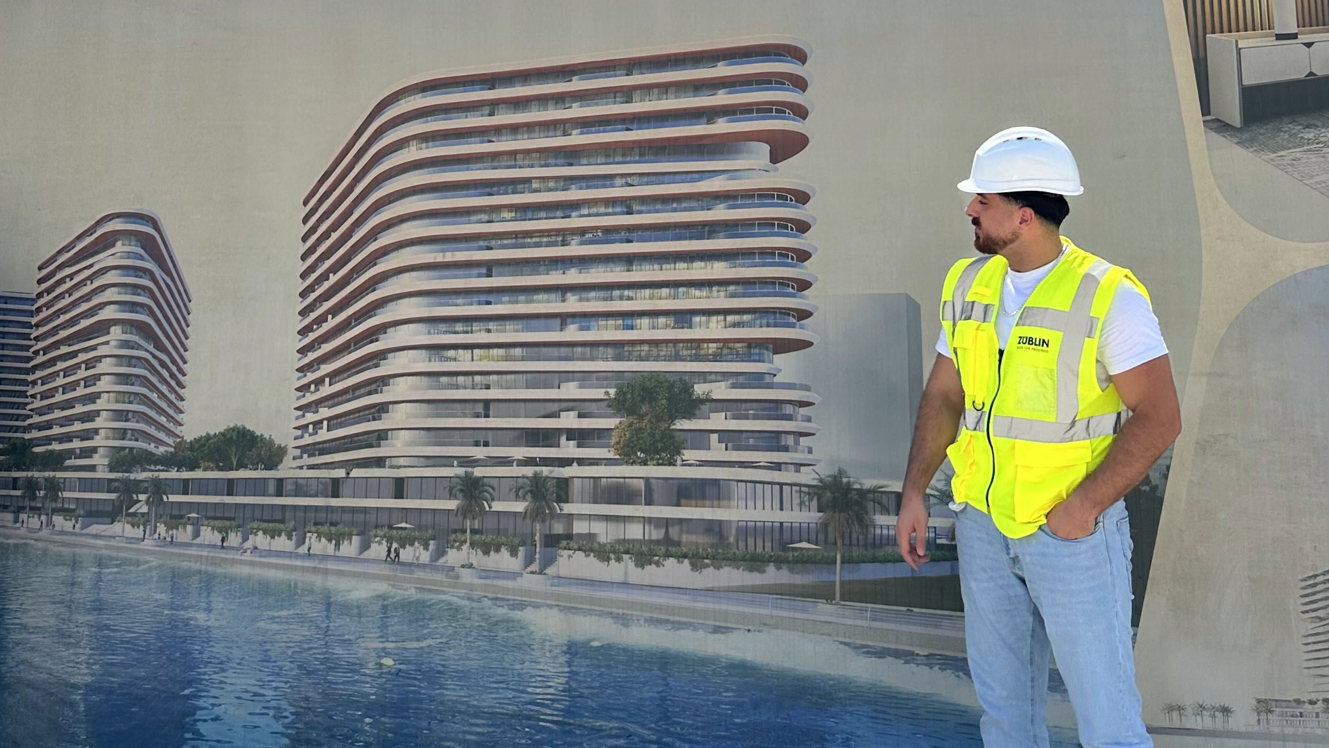 Mann mit Bauhelm und Warnweste steht vor dem Entwurf eines Gebäudes