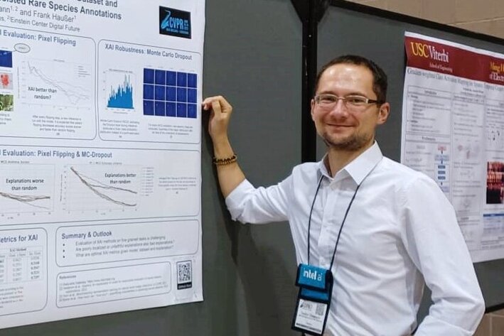 Ein Mann steht an einer Tafel, auf der ein wissenschaftliches Poster befestigt ist