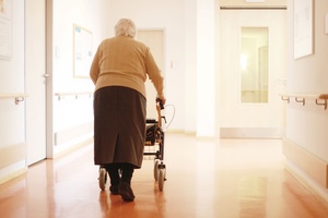 Ein alter Mensch geht mit einem Rollator einen Flur entlang.
