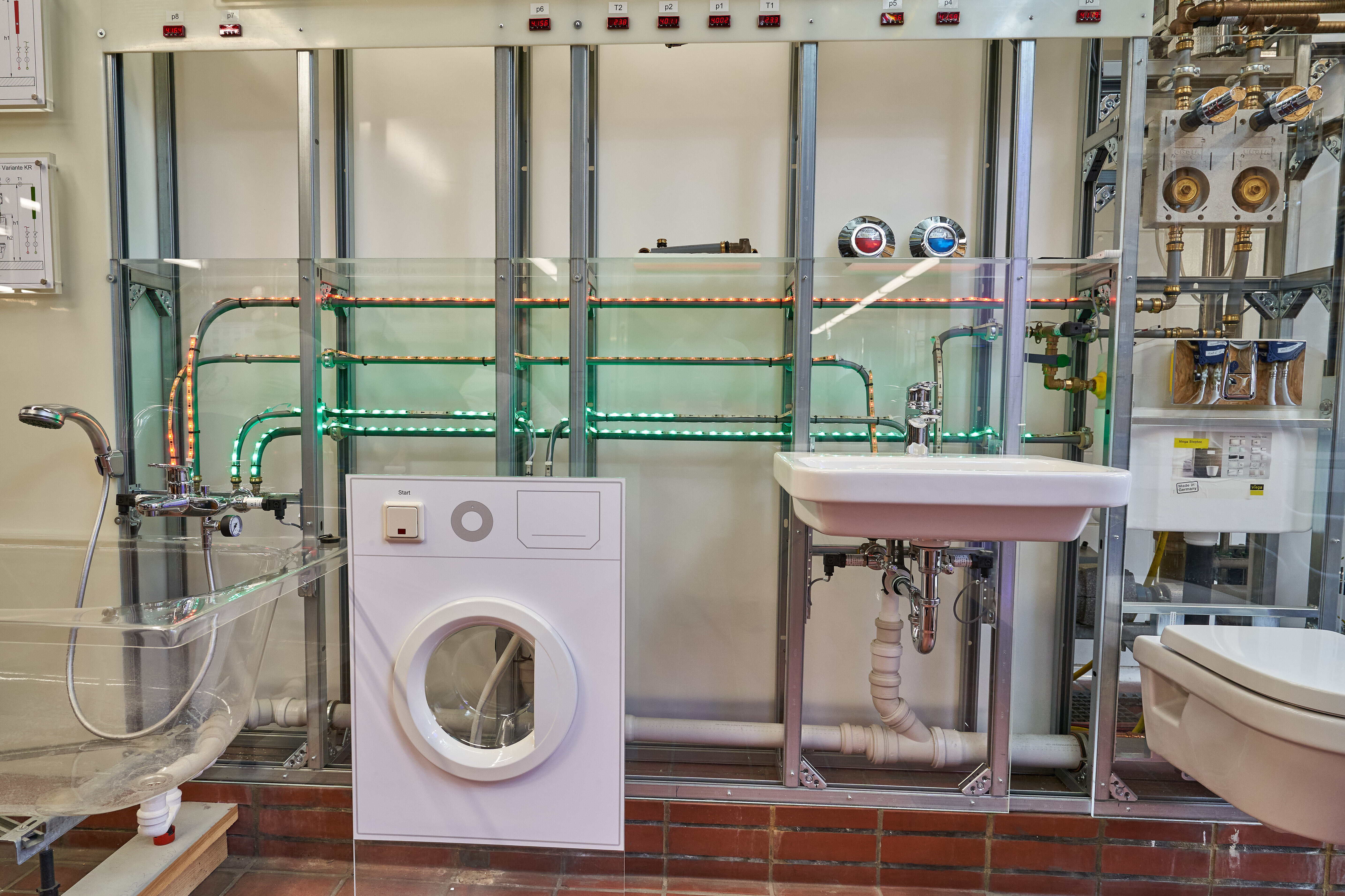 Dusche und transparente Badewanne, Waschmaschinenfront, Waschbecken und Toilette, sichtbare Rohre und Leitungen im Hintergrund